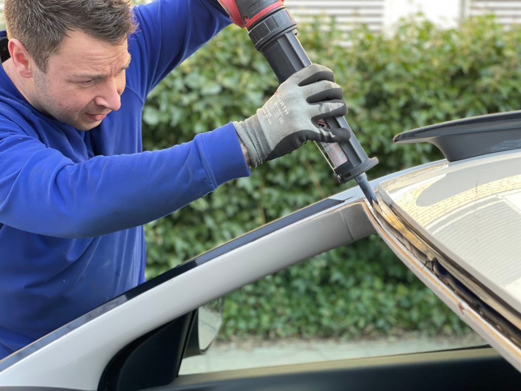 Service worker putting new adhesive onto the windshield area to replace the old windshield.
